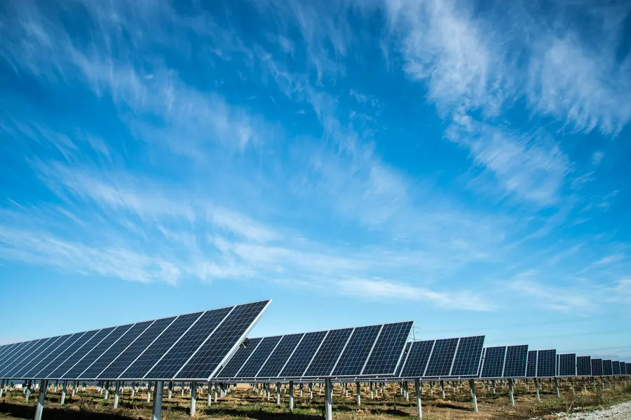 Mavi gökyüzü altında arazi tipi güneş enerjisi santrali panel sıraları